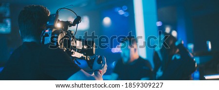 Director of photography with a camera in his hands on the set. Professional videographer at work on filming a movie, commercial or TV series. The filming process indoors, on a concert stage.