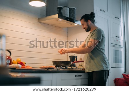 A man prepares breakfast in the kitchen. Young handsome caucasian male preparing food for himself for lunch on a gas stove in a large bright kitchen