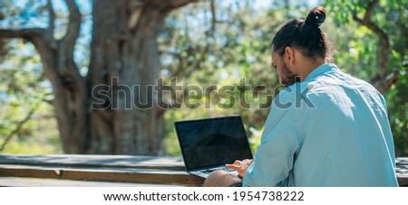 Male tourist working on a laptop outdoors in a camping. Young guy, freelancer working online at a laptop computer on a hike in the mountains outdoors. The ability to work from anywhere in the world. 商業照片 © 