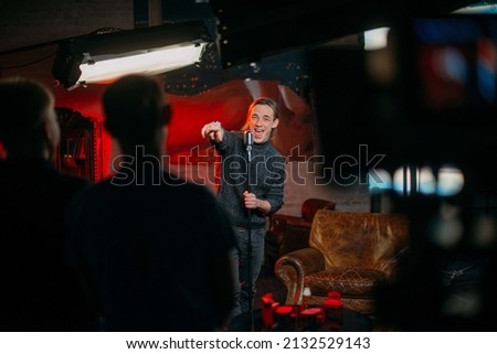 Shooting a stand-up show. Stand-up comedian on stage at the microphone. A young man, an author of jokes and comedy texts, stands on a stage in a studio during the filming of a show. Stockfoto © 