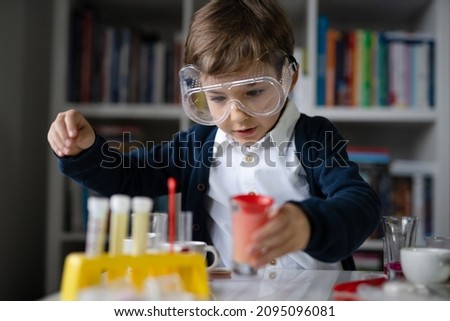 One small caucasian boy scientist five years old wearing protective eyeglasses sitting at the table playing with chemistry equipment toy preforming experiment learning and education concept front view 商業照片 © 