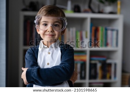 One small caucasian boy scientist five years old wearing protective eyeglasses standing in front of bookshelf looking to the camera learning and education concept front view 商業照片 © 