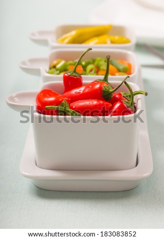 Chili sweet red and pickled green peppers with colorful salad, in food trays on diner table