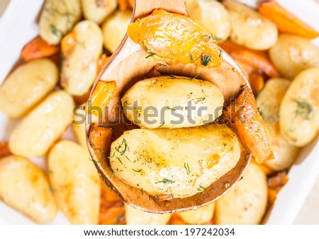 Roasted potatoes with carrot on the wooden ladle above the baking dish
