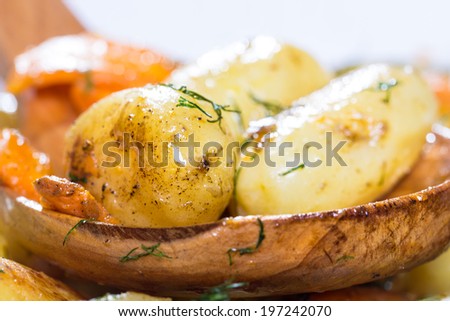 Roasted potatoes with carrot on the wooden ladle above the baking dish
