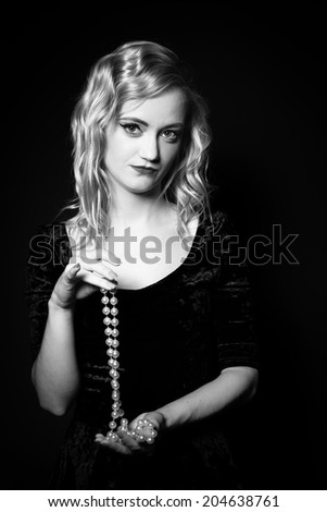 Portrait of attractive blond hair woman with vintage, classic hairstyle and makeup and pearls necklace in studio on the black background