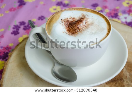 Hot cappuccino coffee scatter over with cinnamon powder on the flower pattern of tablecloth background