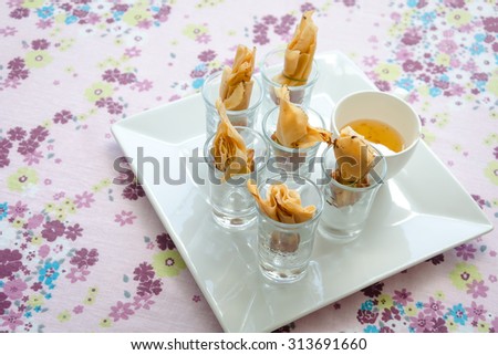 Golden bag stuffed with shrimp and plum sauce on flower pattern of tablecloth background