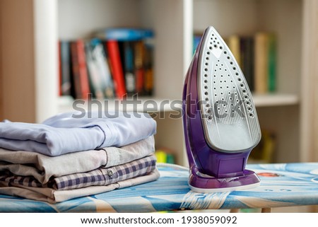 Iron on the ironing board next to a stack of ironed shirts