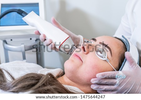 Beautician applying radio frequency microneedling handpiece to a woman's face for skin tightening treatments at a beauty clinic. Stok fotoğraf © 