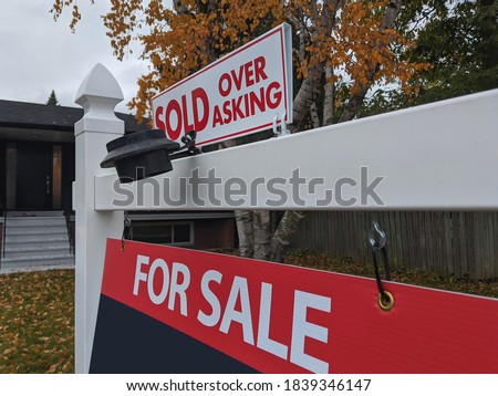 Fresh new sign sold over asking for sale in front of detached house in residential area. Real estate bubble, crash, hot housing market, overpriced property, buyer activity concept. Selective focus.