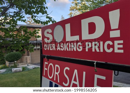 New sign sold over asking price for sale in front of detached house in residential area. Real estate bubble, crash, hot housing market, overpriced property, buyer activity concept. Selective focus.