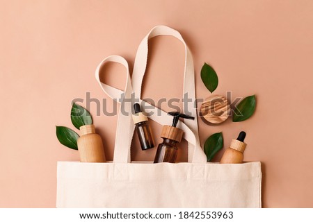 Eco-friendly cotton reusable bag with the different tubes and bottles from the natural wood and brown glass.Fresh natural leafs around.Concept of the organic,zero waste cosmetics.