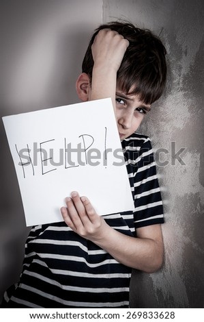 Scared and abused young boy holding the paper with handwritten help sign. Low key
