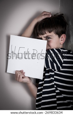 Scared and abused young boy holding the paper with handwritten help sign. Low key