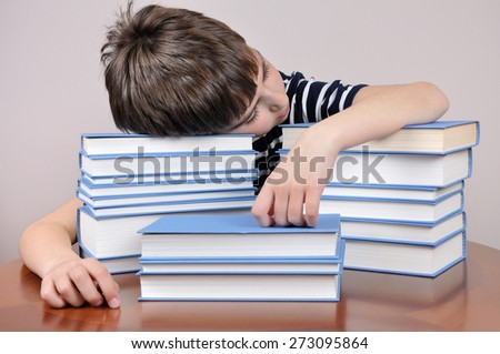 Tired young boy sitting and sleeping at the brown table with his head on the books