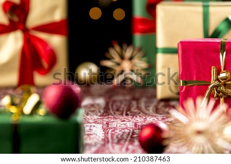 Tightly-framed shot of plain presents in gold and green. Blurred shapes of baubles and stars outside the shallow depth of field. Focus is on the central void and red gift with golden bow.