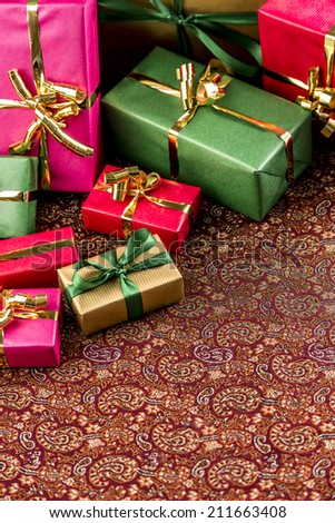 Uni-colored gifts wrapped in red, magenta, green and gold. Tightly framed. Shallow depth of field. Diagonal composition with void foreground. Rich in textures.