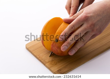 A mango positioned firmly on a cutting board and sliced along the flat side of the core of the fruit. The resulting slice reveals the bright orange pulp of the ripe mango.