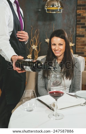 Waiter pouring red wine to a beautiful smiling woman
