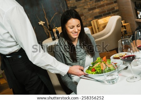 Waiter serving a plate of salad to a woman guest in a restaurant