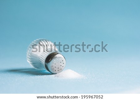 Spilled salt and saltshaker on blue background