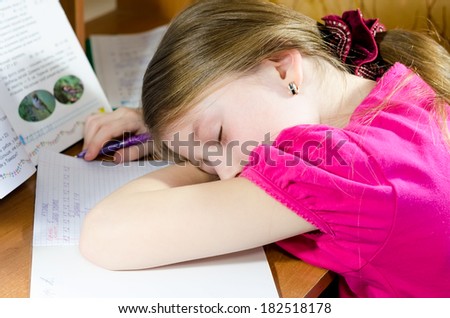 Tired schoolgirl sleeps at the desk