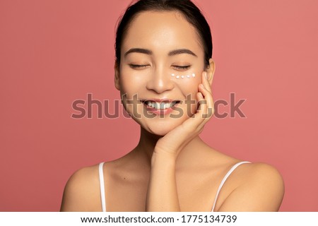 Anti aging eye cream. Young Beautiful model posing aginst pink background with applyed cream under her eyes