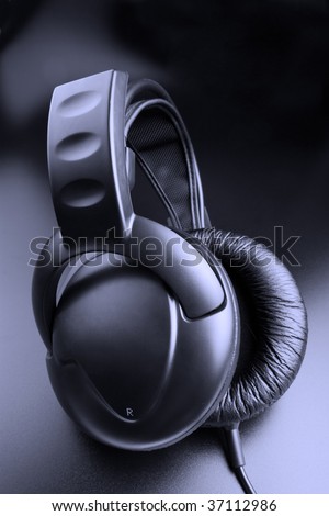Black music - closed black earphones on black background. Blue toned