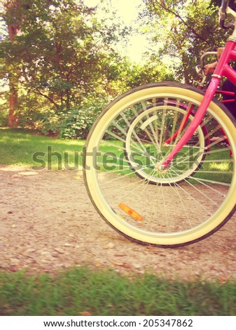 two bikes in motion riding down park path on sunny afternoon with instagram filter Focus is on red bike wheels on further side