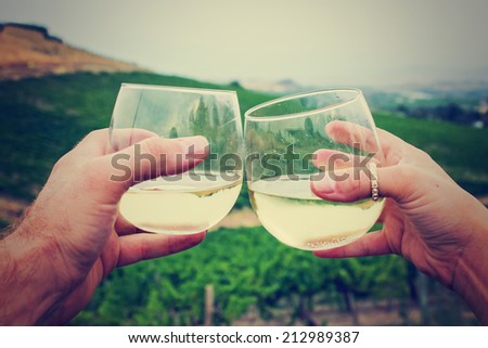 two hands and wine glasses overlooking vineyard at sunset with retro filter