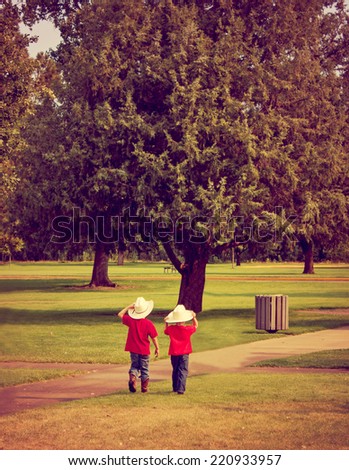 two young boys walking through a park wearing cowboy hats and boots with instagram filter