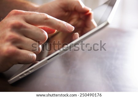 male hand touching tablet with finger tip while holding on a table (shallow depth of field)