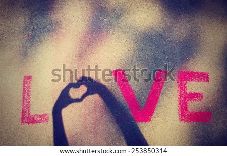 love written with chalk and then a shadow from two hands displays the O in the work with a heart with a instagram filter (shallow depth of field)