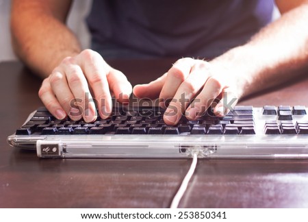 man typing at a tabletop with a black keyboard with a drama filter (shallow depth of field)