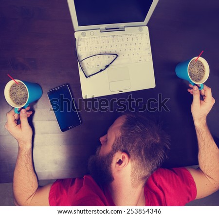 mans head down on a tabletop while holding two cups of coffee while working at a desk on laptop with an instagram filter