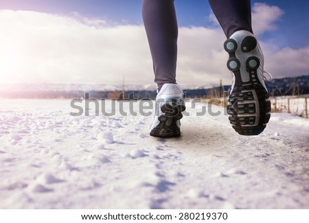 woman running on a snowy country road with view of the snow covered mountains on an afternoon day with sun flare (shallow depth of field)