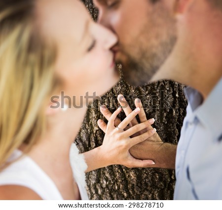 man and woman kissing with focus on hands against tree trunk with shallow depth of field