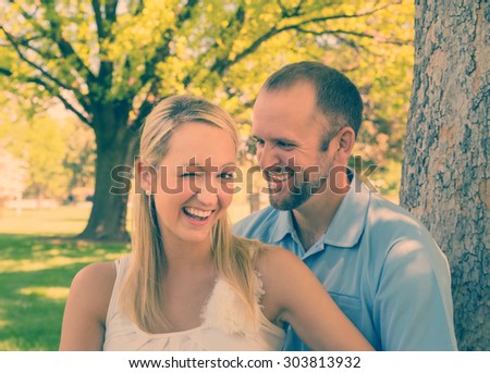 couple sitting beside a tree in a park with goofy faces with an instagram filter