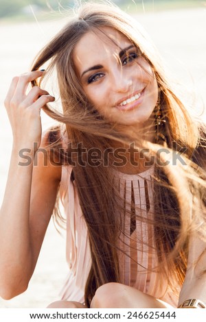 Close up fashion portrait of a beautiful woman with big eyes and full lips and white teeth  in evening dress with windy long hair . She smiling and having fun in the rays of the setting sun.