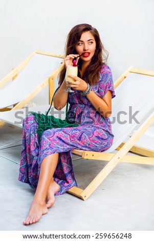 Wonderful sexy woman relaxing and drink cocktail  in luxury spa wearing long colorful dress. lady sitting on deck chair and Enjoying vacation.