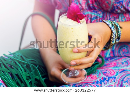 Close up fashion outdoor portrait of elegant   sensual woman boho dress and colorful stylish accessories. Focus on hands holding  tropical cocktail  with exotic  flower .