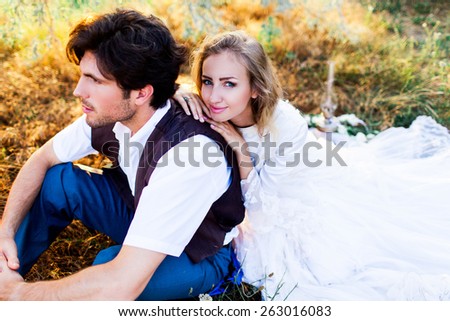 Close up fashion portrait of young beautiful  couple in love . bride and groom sitting  and enjoying sunset. Man wearing stylish retro vest and lady in white dress. Focus on bride face.Film colors.
