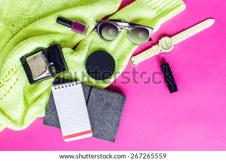 Top view of  trendy   spring  accessories  of modern woman on pink floor. Neon sweater , yellow wrist watch,glasses, lipstick, nail polish, perfume, electronic book and notepad. multicolor  mood.