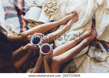 Soft photo of two women on the bed with old books and cup of tea  in hands wearing cozy sweater , top view point. Two  best friends enjoying  morning.