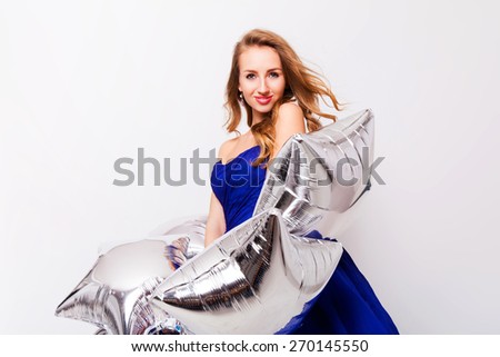 Beautiful young blonde  student celebrate prom and holding  silver party balloons. Wearing blue evening elegant dress and have day of.