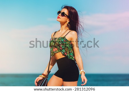 Perfect fit  girl  in trendy cool sunglasses   with  tan  body  posing on the tropical  beach wearing bright colored top, hight shorts and stylish swag accessories .