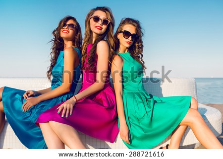 Three  pretty  friends in  same  colorful  dresses   posing  near the beach, wearing stylish sunglasses and enjoying  vacation in summer city. Bright colors.