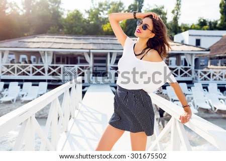 Elegant pretty slim woman in trendy summer outfit posing near luxury resort near the beach . Wearing stylish shirt high skirt and white t-shirt .