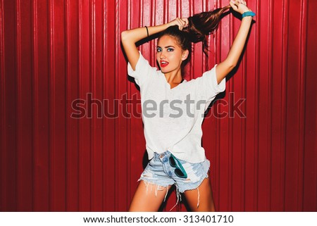 Young  pretty crazy  hipster woman in trendy autumn clothes have fun and doing grimaces  near red  background  urban style  on  night party.  Bright flash ,  contrast color .